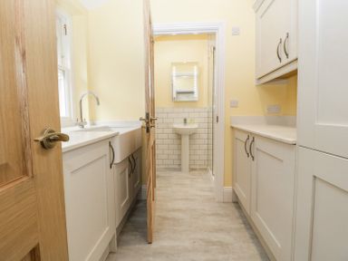 A utility room with cabinets a sink and an open door leading to a bathroom with a pedestal sink and mirror at Belle Vue in Hay on Wye Herefordshire