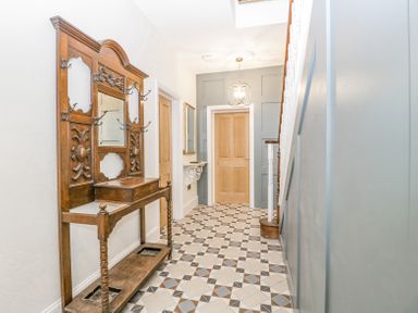 A hallway with patterned tile floor a wooden coat rack with hooks a mirror wooden doors a wall-mounted shelf and stairs at Belle Vue in Hay on Wye Herefordshire