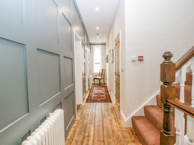 A hallway with wooden floorboards a patterned runner a wooden chair at the end and carpeted stairs with a wooden banister at Belle Vue in Hay on Wye Herefordshire