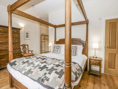 A bedroom with a wooden four-poster bed two bedside tables with lamps a wooden chest of drawers a wooden chair and an open clothes rack at Belle Vue in Hay on Wye Herefordshire
