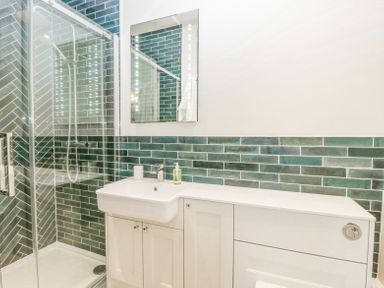 A bathroom with a shower enclosure a sink with cabinet and green tiled walls at Belle Vue in Hay on Wye Herefordshire