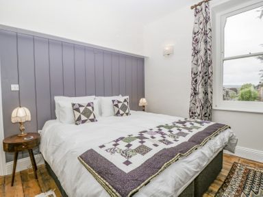 A bedroom with a large bed two bedside tables with lamps a window with patterned curtains and wooden flooring at Belle Vue in Hay on Wye Herefordshire