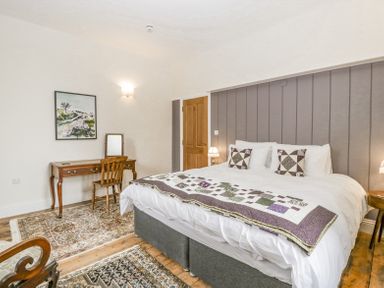 A bedroom with a large bed two patterned pillows a wooden desk and chair and rugs on the floor at Belle Vue in Hay on Wye Herefordshire