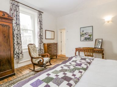 A bedroom with a wooden rocking chair a chest of drawers a desk with a chair and a bed with a quilt at Belle Vue in Hay on Wye Herefordshire