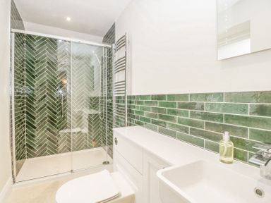 A bathroom with a glass shower enclosure green tiled walls white sink and toilet at Belle Vue in Hay on Wye Herefordshire