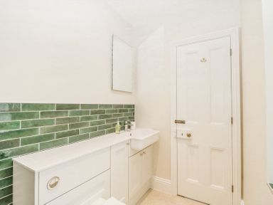 A bathroom with green subway tiles on the wall a white cabinet with a sink a mirror and a closed white door at Belle Vue in Hay on Wye Herefordshire