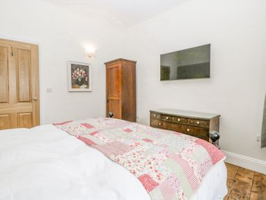 A bedroom with a bed covered with a patchwork quilt a wooden wardrobe a wooden dresser with a glass top a wall-mounted television and a painting at Belle Vue in Hay on Wye Herefordshire