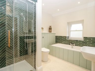 A bathroom with a glass shower enclosure green tiled walls a bathtub toilet and sink at Belle Vue in Hay on Wye Herefordshire