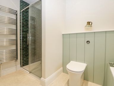 A bathroom with a toilet shower with green tiles and a chrome towel radiator at Belle Vue in Hay on Wye Herefordshire