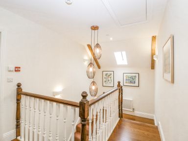 A stair landing with wooden handrails and spindles three pendant lights framed pictures on walls and a skylight at Belle Vue in Hay on Wye Herefordshire
