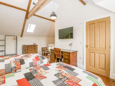 A bedroom with two beds covered in patchwork quilts a wooden desk with chair a wall-mounted television a chest of drawers and wooden ceiling beams at Belle Vue in Hay on Wye Herefordshire