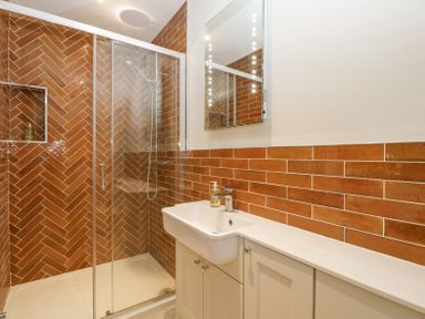 A bathroom with a glass shower enclosure white sink and brown tiled walls at Belle Vue in Hay on Wye Herefordshire