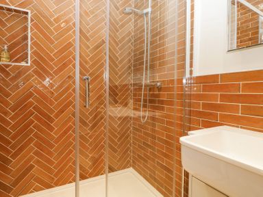 A bathroom with a glass shower enclosure brown tiled walls and a white sink at Belle Vue in Hay on Wye Herefordshire