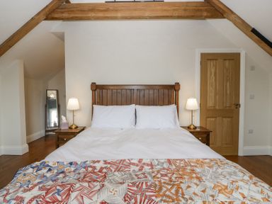 A bedroom with a wooden bed frame white bedding two bedside tables with lamps a wooden door and a standing mirror at Belle Vue in Hay on Wye Herefordshire