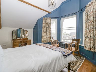 A bedroom with a bed a wooden dressing table with mirror two chairs by windows with patterned curtains at Belle Vue in Hay on Wye Herefordshire