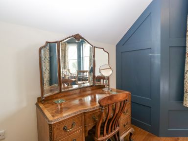 A wooden dressing table with a three-panel mirror and chair in a room with blue paneled wall at Belle Vue in Hay on Wye Herefordshire
