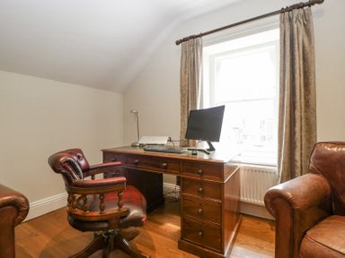 A home office with a wooden desk computer monitor keyboard laptop leather chair and window with curtains at Belle Vue in Hay on Wye Herefordshire