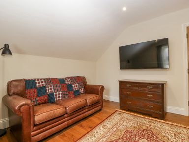 A room with a brown leather sofa with a patchwork blanket a wooden dresser a wall-mounted TV and a patterned rug at Belle Vue in Hay on Wye Herefordshire