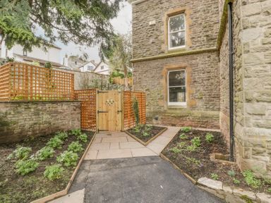 An outdoor garden area with flower beds wooden fence and gate beside a stone building at Belle Vue in Hay on Wye Herefordshire
