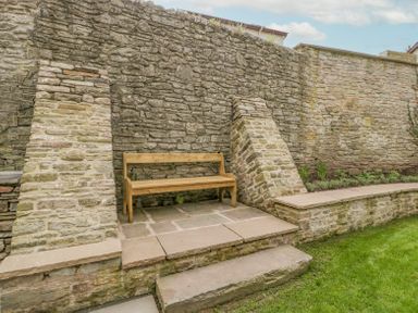 A wooden bench on a stone patio against a stone retaining wall in a garden at Belle Vue in Hay on Wye Herefordshire