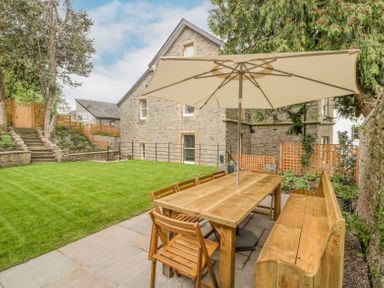 An outdoor patio area with a wooden table and chairs under a large umbrella beside a stone house at Belle Vue in Hay on Wye Herefordshire
