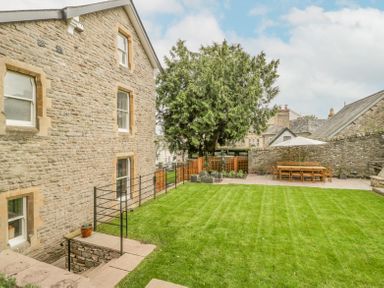 A stone house with a green lawn and outdoor dining table with umbrella in a garden at Belle Vue in Hay on Wye Herefordshire