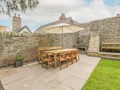 An outdoor patio with a wooden table and chairs under a white umbrella beside stone walls and a small grassy area at Belle Vue in Hay on Wye Herefordshire