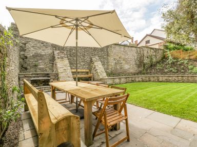 A patio area with a wooden table chairs and bench under a large umbrella adjacent to a stone wall and lawn at Belle Vue in Hay on Wye Herefordshire