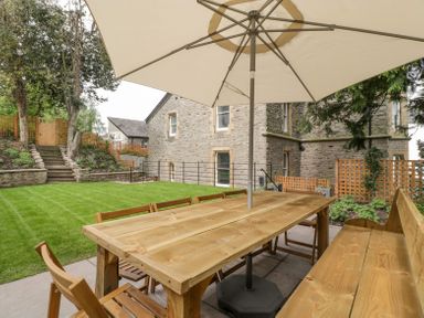 A backyard with a wooden table umbrella chairs and a bench on a patio at Belle Vue in Hay on Wye Herefordshire