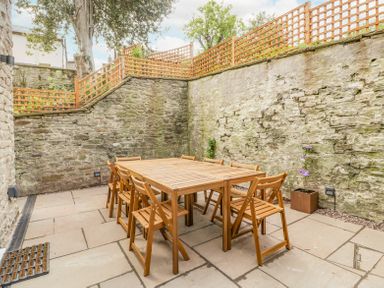 An outdoor patio area with a wooden dining table and chairs surrounded by stone walls and wooden lattice fencing at Belle Vue in Hay on Wye Herefordshire