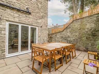 A stone patio with wooden outdoor dining table and chairs near glass doors at Belle Vue in Hay on Wye Herefordshire