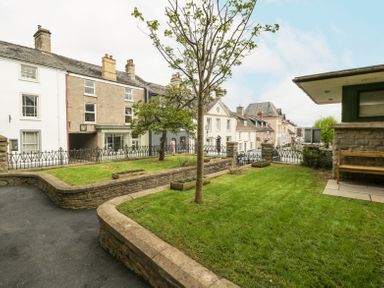 A garden with a tree and planters next to a paved path and a wooden bench at Belle Vue in Hay on Wye Herefordshire