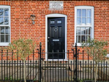 A black door and two windows on a red brick building with a black metal fence and two small trees at Ebenezer Chapel in Knodishall nr Saxmundham