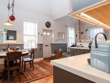 A dining area with a round table set for a meal and kitchen counter with appliances at Ebenezer Chapel in Knodishall nr Saxmundham