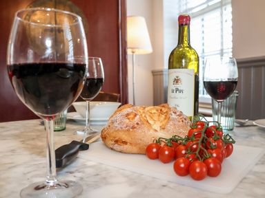 A dining table with a loaf of bread cherry tomatoes a bottle of red wine and glasses of red wine at Ebenezer Chapel in Knodishall nr Saxmundham
