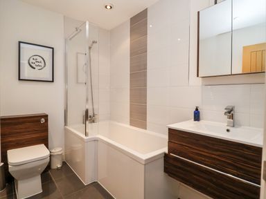A bathroom with a toilet, bathtub with shower, and sink with mirror cabinet at Ebenezer Chapel in Knodishall nr Saxmundham