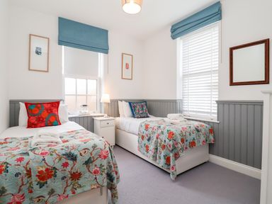 A bedroom with two single beds each with floral bedspreads and cushions a nightstand between the beds and windows with blue blinds at Ebenezer Chapel in Knodishall nr Saxmundham
