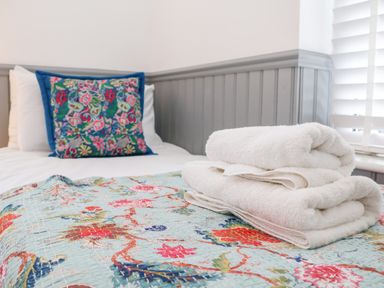 A bed with white towels folded on a floral quilt and a pillow with a colorful embroidered cover at Ebenezer Chapel in Knodishall nr Saxmundham