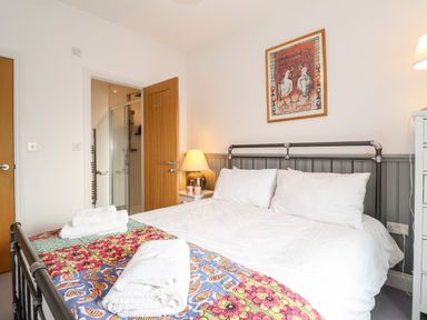 A bedroom with a metal bed frame white bedding colorful quilt towels bedside lamp and a framed picture above the bed at Ebenezer Chapel in Knodishall nr Saxmundham