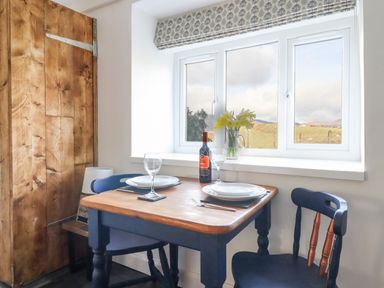 A small dining table set for two by a window with a bottle of wine and flowers at Ael Y Bryn in Ffestiniog