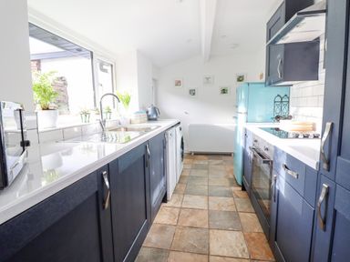 A kitchen with blue cabinets a blue refrigerator a window with plants and a tiled floor at Ael Y Bryn in Ffestiniog