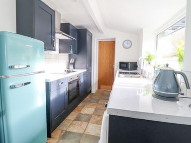 A kitchen with blue cabinets a turquoise fridge and kettle a microwave sink and wooden door at Ael Y Bryn in Ffestiniog
