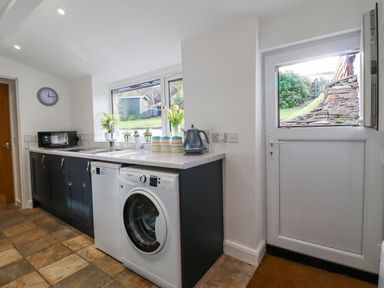 A kitchen area with washing machine microwave sink and kettle next to a door at Ael Y Bryn in Ffestiniog