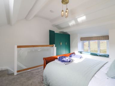A bedroom with a bed next to a window with cushions and a green wardrobe at Ael Y Bryn in Ffestiniog