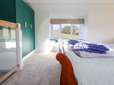 A bedroom with a wooden bed a window with a patterned valance green wardrobes and folded towels on the bed at Ael Y Bryn in Ffestiniog