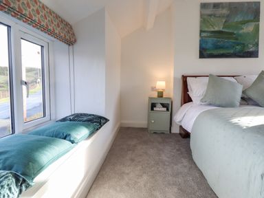 A bedroom with a bed and cushions a bedside table with a lamp and a window seat with cushions at Ael Y Bryn in Ffestiniog
