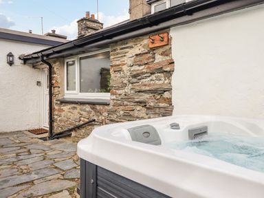 An outdoor stone patio area with a hot tub beside a stone and white plaster wall at Ael Y Bryn in Ffestiniog