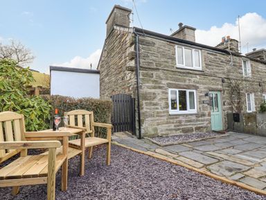 Exterior of a stone house with blue door and wooden chairs with table outside at Ael Y Bryn in Ffestiniog