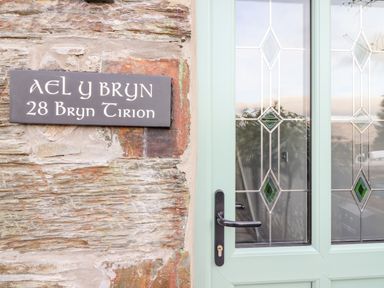 A stone wall with a sign reading Ael Y Bryn 28 Bryn Tirion next to a green door with decorative glass panes at Ael Y Bryn in Ffestiniog