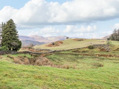 A grassy field with trees stone fences and hills under a cloudy sky at Ael Y Bryn in Ffestiniog